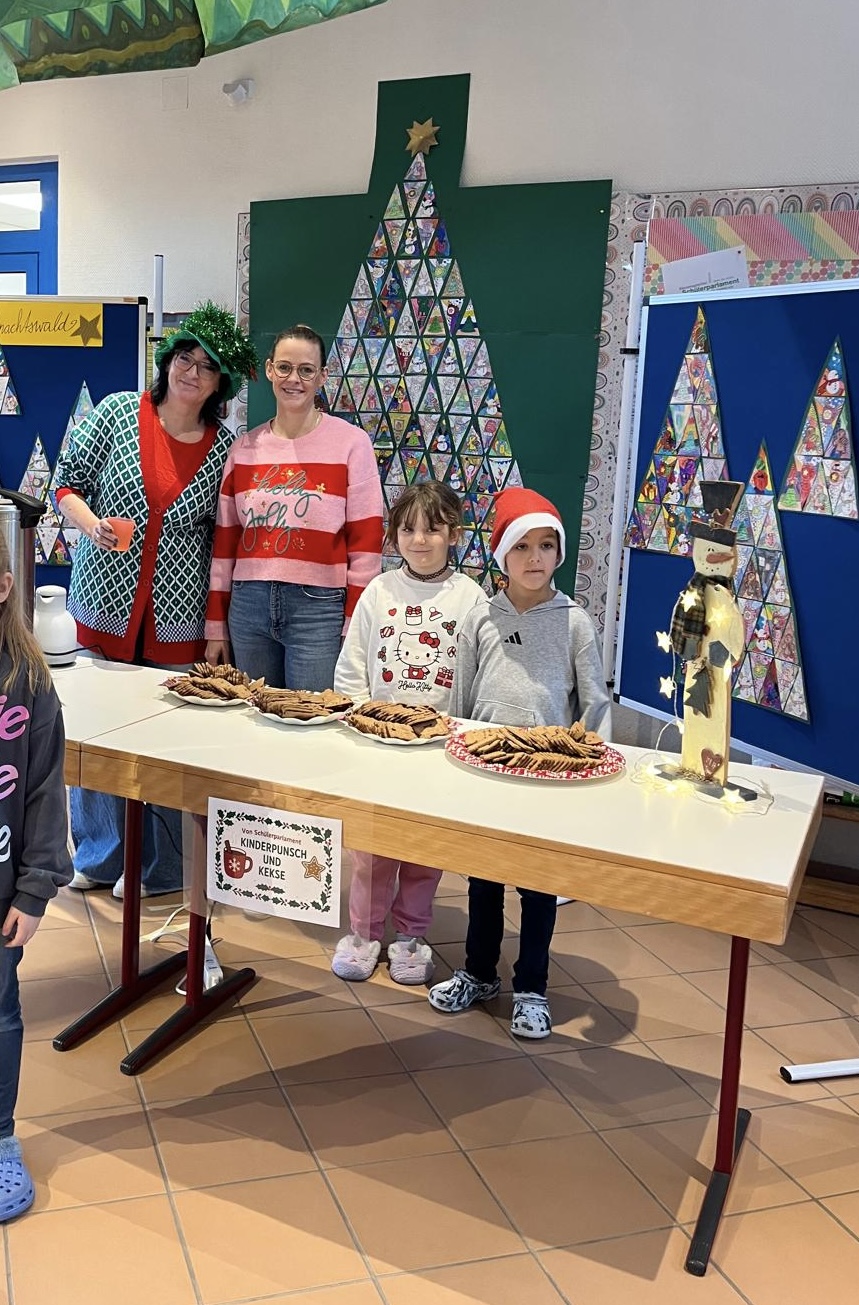 Festlich dekorierter Tisch mit Keksen und Kinderpunsch vor bunten Weihnachtsbaum- und Schneemann-Dekorationen, im Hintergrund stehen mehrere Personen.